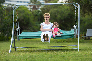 Image showing mother and little daughter swinging at backyard