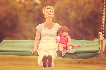 Image showing mother and little daughter swinging at backyard