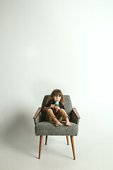 Image showing Little child sitting and playing in armchair on white studio background