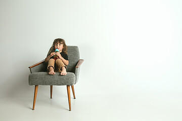 Image showing Little child sitting and playing in armchair on white studio background