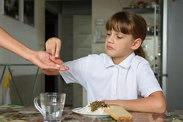 Image showing To a sick girl before a meal, mother holds out medicine in her palm