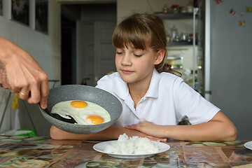 Image showing Mom cooked scrambled eggs for lunch and puts them from the pan on the daughter\'s plate