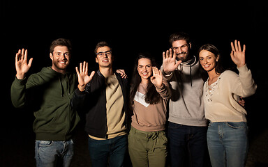 Image showing happy smiling friends waving hands at night