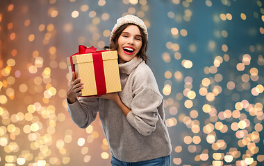 Image showing young woman in knitted winter hat holding gift box