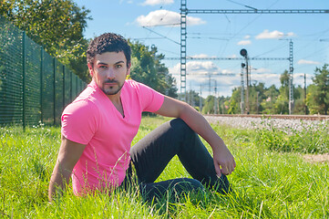 Image showing Young man in orange sitting on the green grass