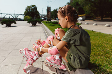 Image showing Teenage girl in a helmet learns to ride on roller skates outdoors