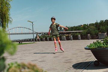 Image showing Teenage girl in a helmet learns to ride on roller skates outdoors