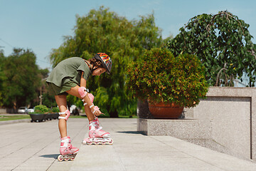 Image showing Teenage girl in a helmet learns to ride on roller skates outdoors