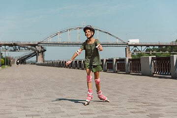 Image showing Teenage girl in a helmet learns to ride on roller skates outdoors