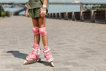 Image showing Teenage girl in a helmet learns to ride on roller skates outdoors