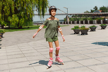 Image showing Teenage girl in a helmet learns to ride on roller skates outdoors