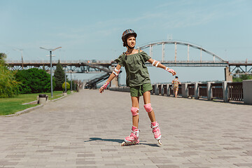 Image showing Teenage girl in a helmet learns to ride on roller skates outdoors