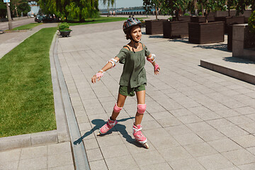 Image showing Teenage girl in a helmet learns to ride on roller skates outdoors