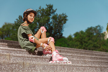 Image showing Teenage girl in a helmet learns to ride on roller skates outdoors