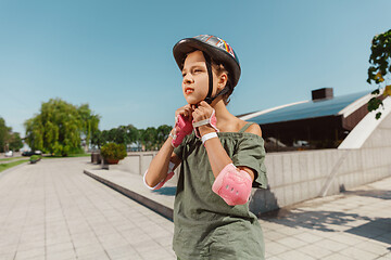 Image showing Teenage girl in a helmet learns to ride on roller skates outdoors