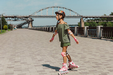 Image showing Teenage girl in a helmet learns to ride on roller skates outdoors