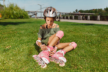 Image showing Teenage girl in a helmet learns to ride on roller skates outdoors