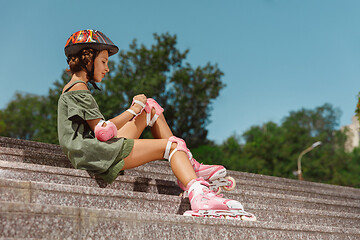 Image showing Teenage girl in a helmet learns to ride on roller skates outdoors