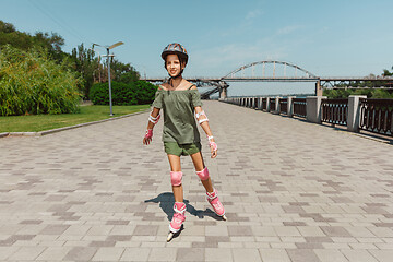 Image showing Teenage girl in a helmet learns to ride on roller skates outdoors