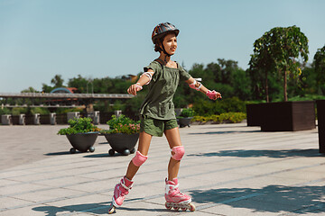 Image showing Teenage girl in a helmet learns to ride on roller skates outdoors