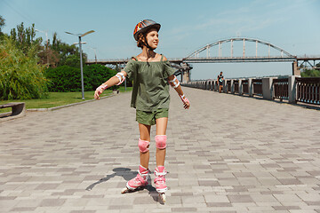 Image showing Teenage girl in a helmet learns to ride on roller skates outdoors