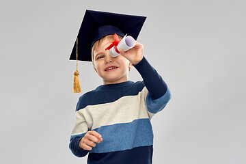 Image showing little boy in mortarboard looking through diploma