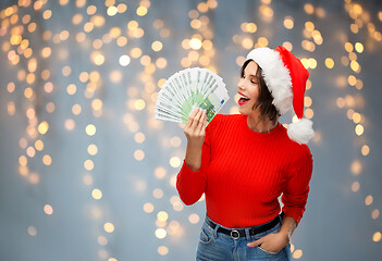 Image showing happy woman in santa hat with money on christmas