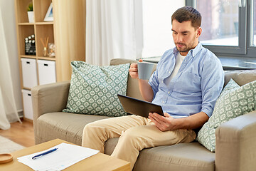 Image showing smiling man with tablet pc drinking coffee at home