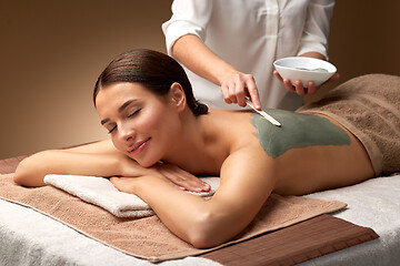 Image showing woman and cosmetologist applying clay mask in spa