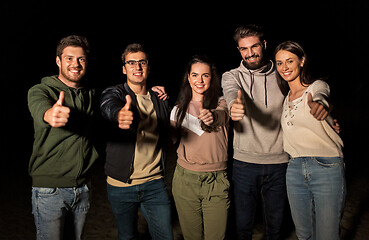 Image showing happy smiling friends showing thumbs up at night