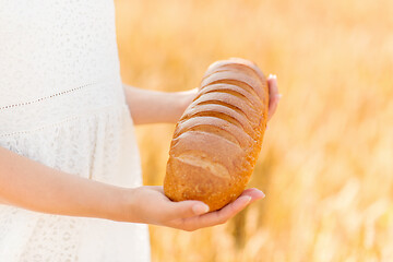 Image showing hands holding loaf of white bread on cereal field