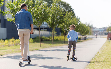 Image showing happy father and little son riding scooter in city