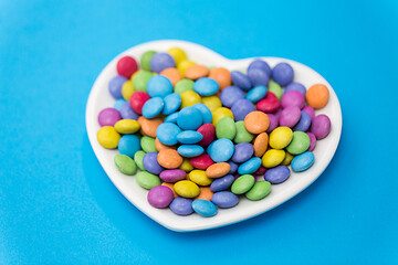 Image showing candies on heart shaped plate over blue background