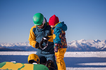 Image showing father preparing his little son for the first time on a snowboar