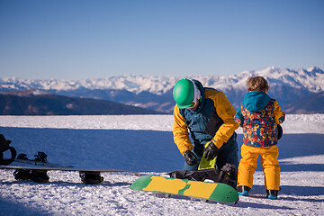 Image showing father preparing his little son for the first time on a snowboar