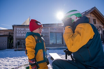 Image showing father preparing his little son for the first time on a snowboar