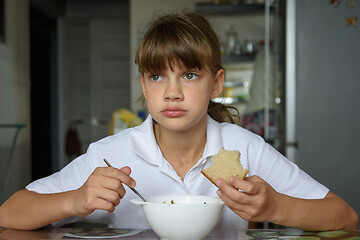 Image showing Girl thoughtfully eats soup at the table in the kitchen