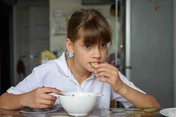 Image showing Tired hungry schoolgirl eating soup at the table in the kitchen