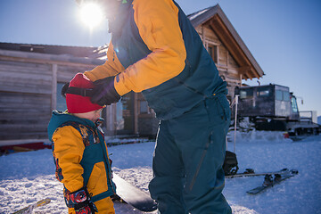 Image showing father preparing his little son for the first time on a snowboar