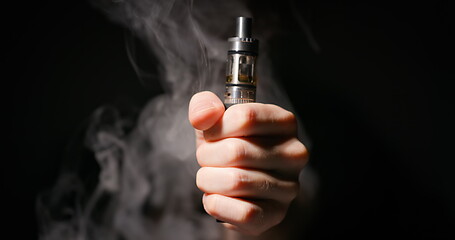 Image showing Electronic cigarette grabbed by male hand against dark background and vapor