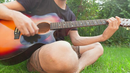 Image showing Man sitting in the grass playing guitar