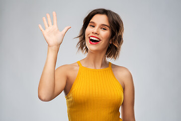 Image showing happy smiling young woman waving hand