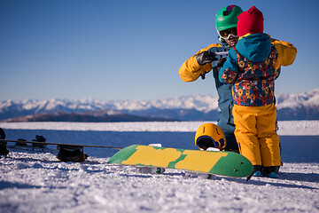 Image showing father preparing his little son for the first time on a snowboar