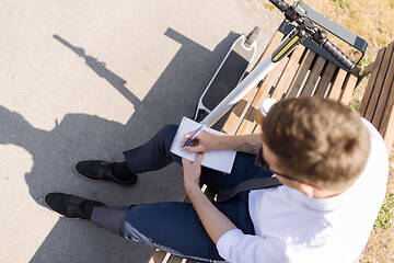 Image showing smiling businessman writing to notebook in city