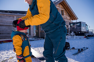 Image showing father preparing his little son for the first time on a snowboar