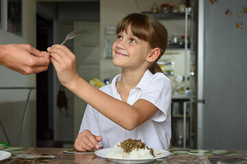 Image showing A girl takes a fork from her mother\'s hand while preparing to dine at the kitchen table