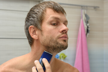 Image showing A man smooths his beard on his face with a hair clipper