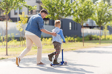 Image showing happy father and little son riding scooter in city