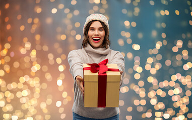 Image showing young woman in knitted winter hat holding gift box