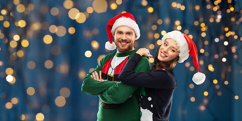 Image showing happy couple in christmas sweaters and santa hats